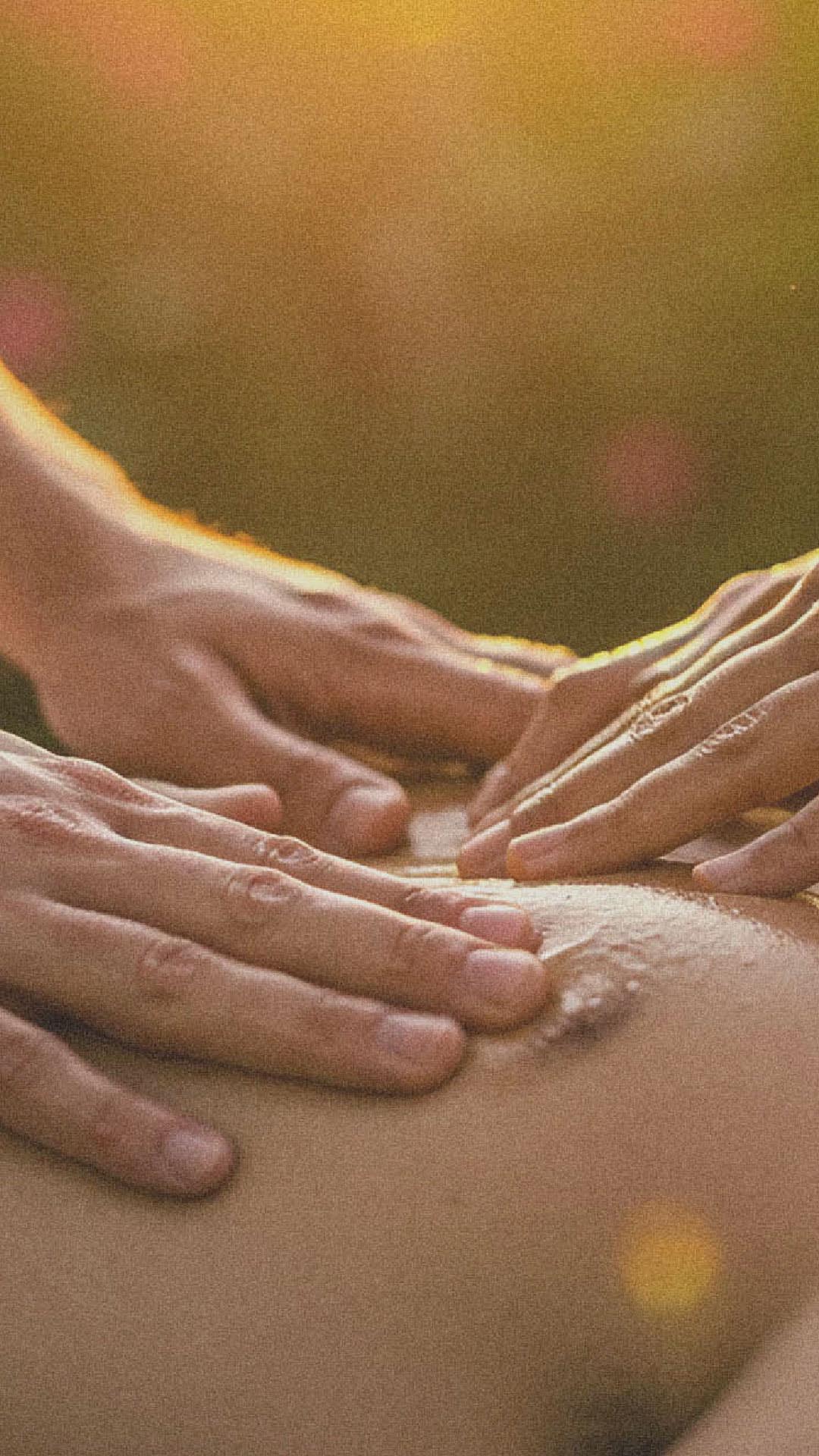Tantra Massage Workshop Close-up of hands gently massaging a person's back in warm sunset light