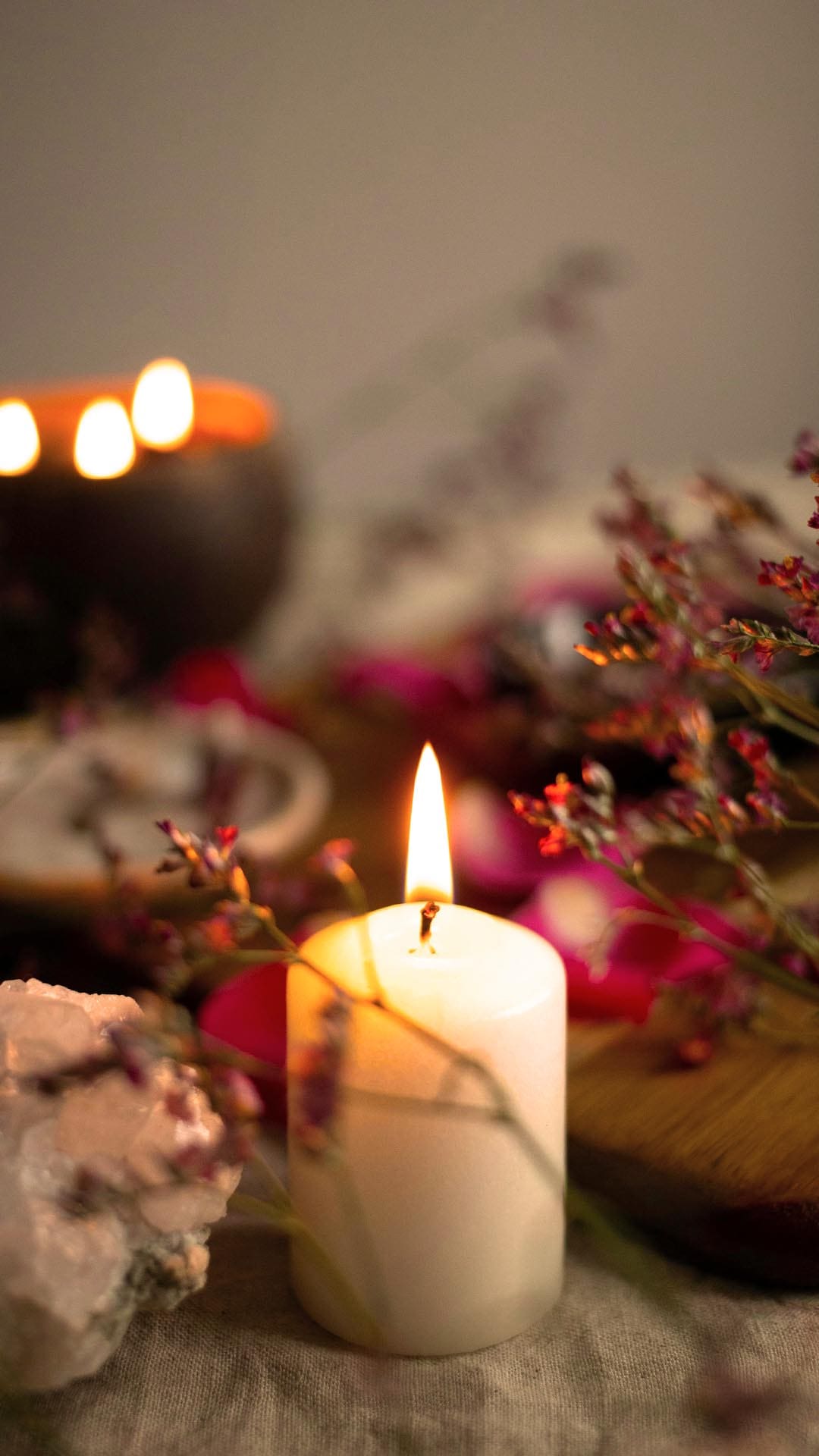 Tantric Rituals for Beginners: Create a Warm Sacred Space at Home Lit white candle surrounded by flowers and crystals, creating a peaceful sacred space for tantric rituals at home.
